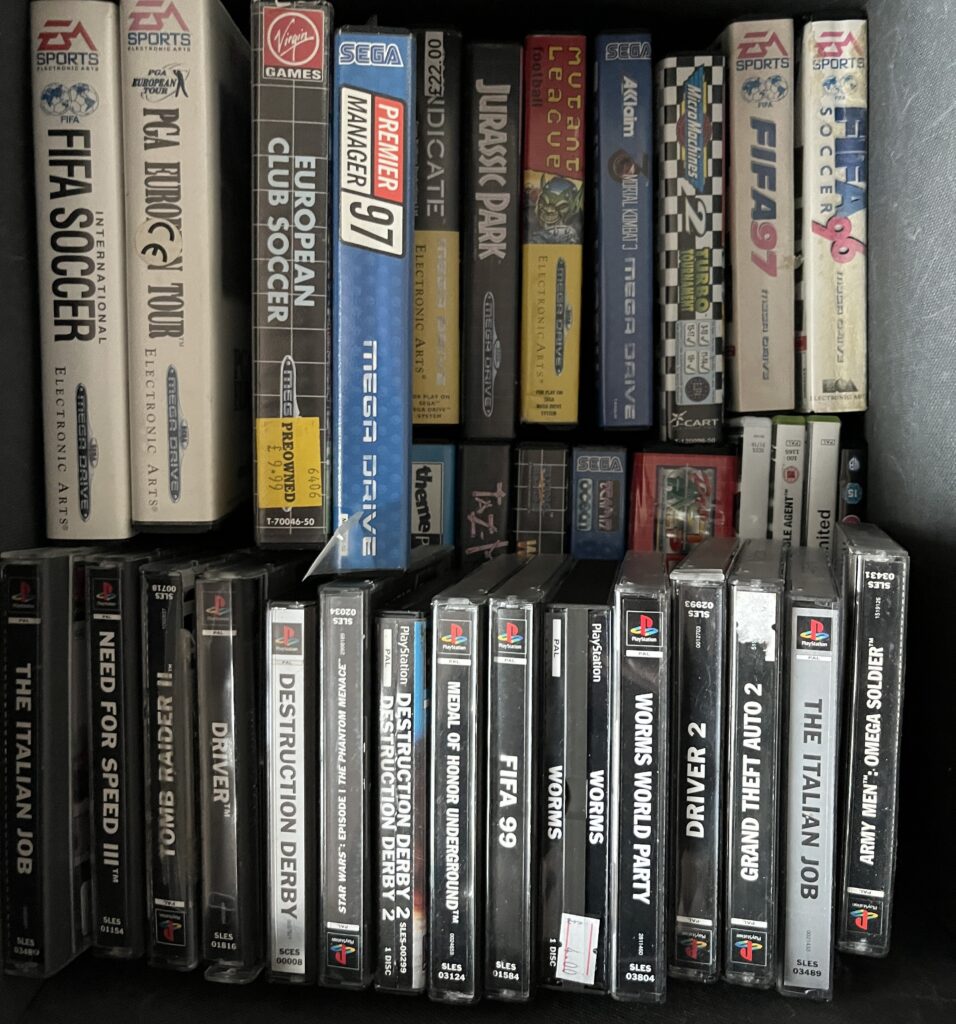 Box of Mega Drive cartridge boxes above PS1 jewel cases, arranged like a small home library.