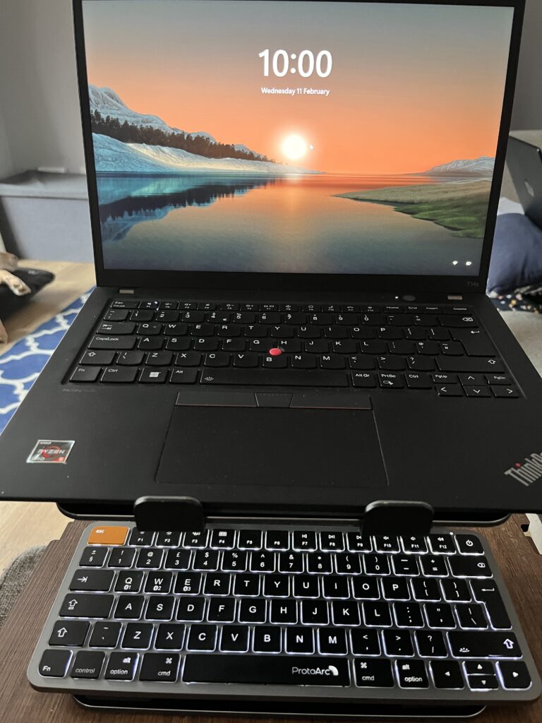 backlit compact keyboard ThinkPad laptop raised on a stand with the ProtoArc backlit keyboard positioned below for lap tray typing