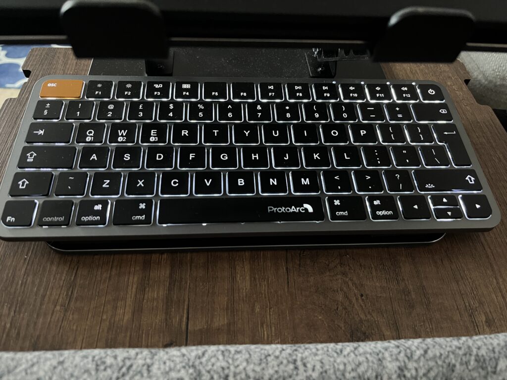 ProtoArc K90-A compact keyboard with the backlight turned on, sitting on a wooden lap tray