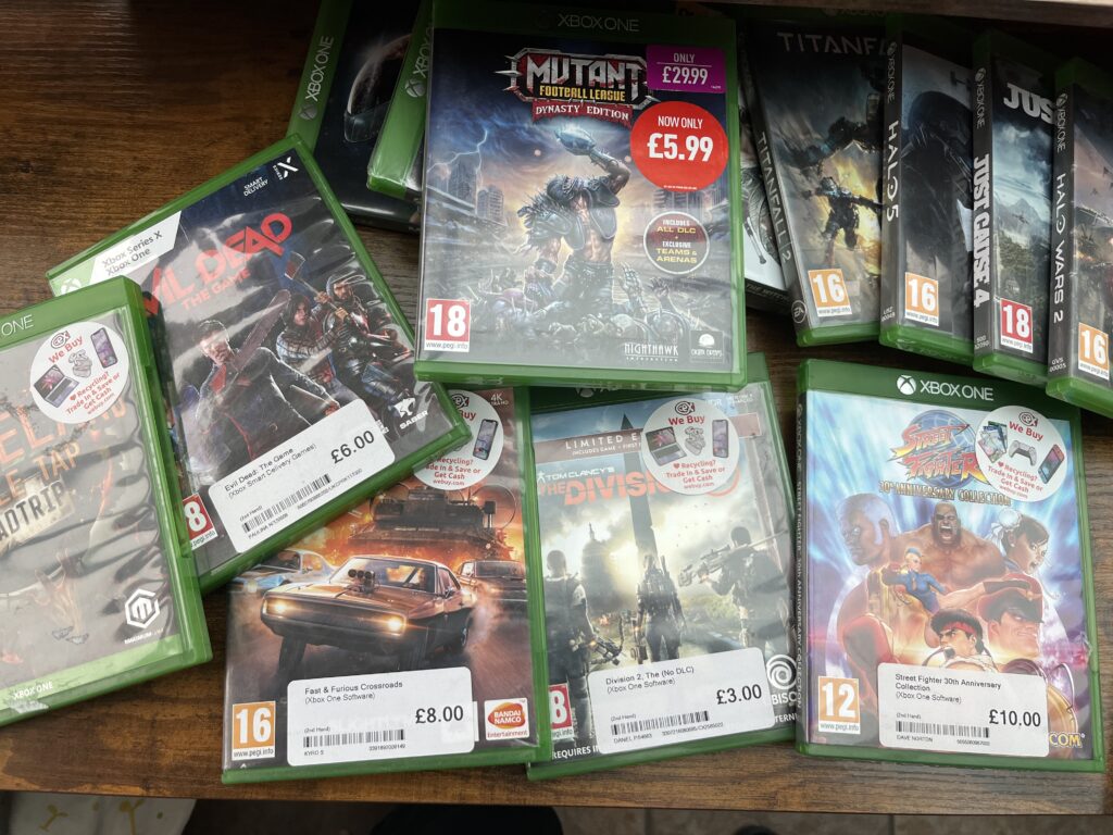 Stepping back from Game Pass Pile of used Xbox One game cases with price stickers, including The Division 2, Evil Dead: The Game and Street Fighter 30th Anniversary Collection.