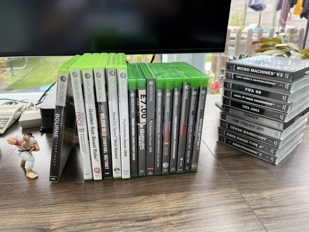 A tall, diverse stack of console games including Xbox One, Xbox 360, and PlayStation 1 cases.